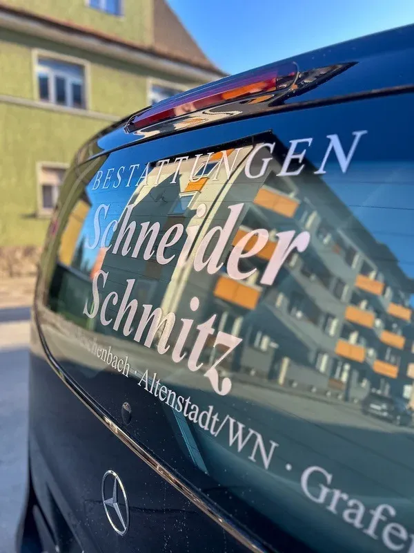 Heckscheibe des Bestattungsfahrzeugs mit dem Schriftzug „Bestattungen Schneider Schmitz“.