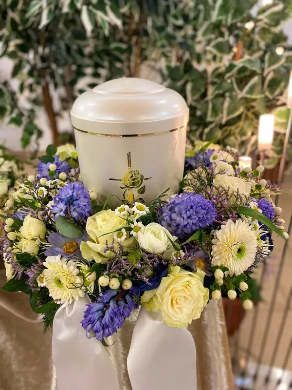 Weiße Urne mit einem Kranz aus blauen Hyazinthen, weißen Rosen und Kamille.