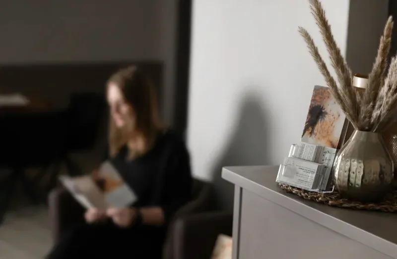 Ruhiger Wartebereich: im Vordergrund Pampasgras in einer goldenen Vase, im Hintergrund eine lesende Person.